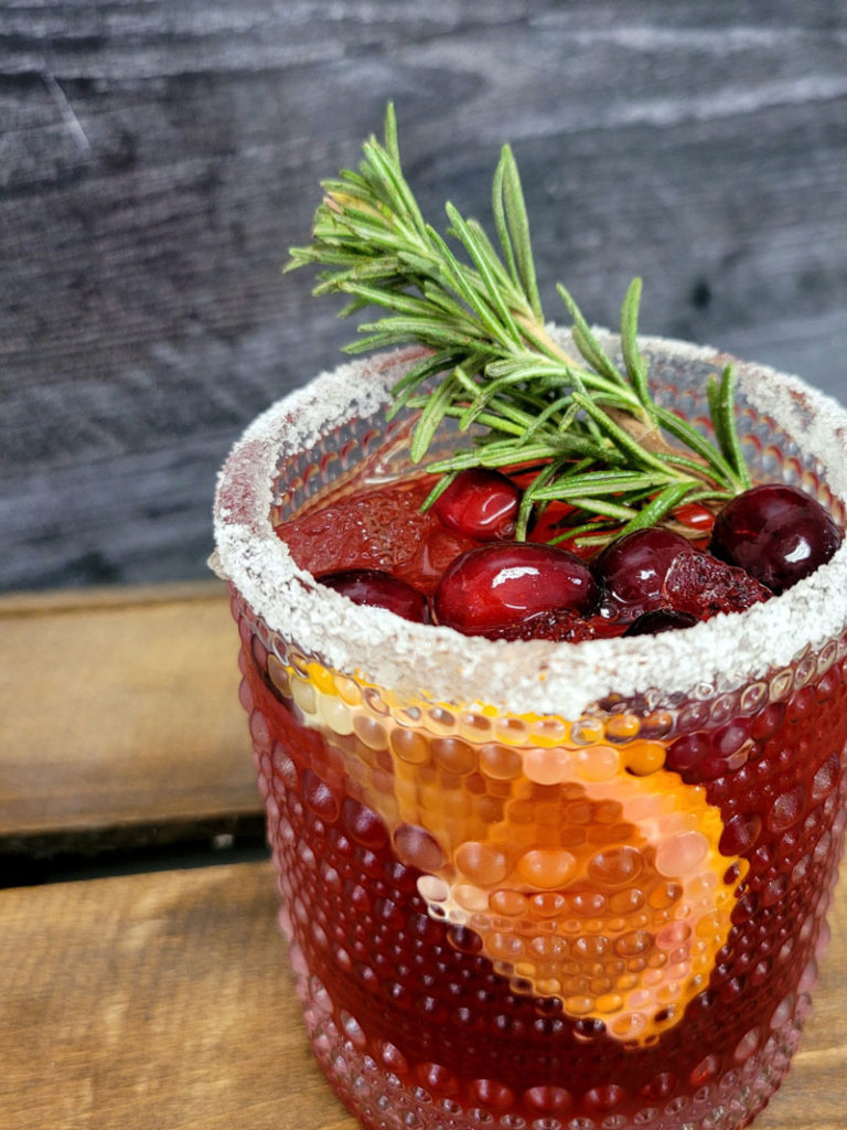 merry merry margarita, a red cocktail garnished with rosemary, cranberries, and an orange slice
